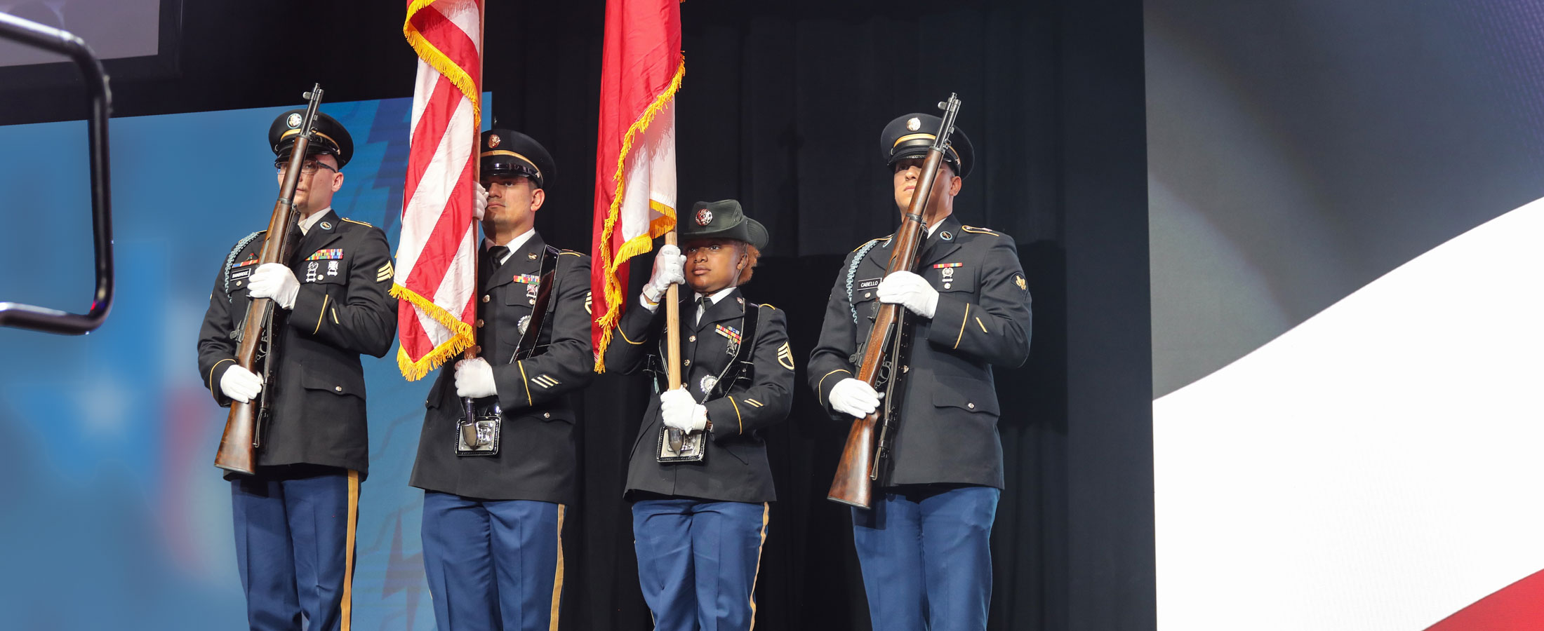 Four military personnel are standing and presenting the American flag and the Texas flag.